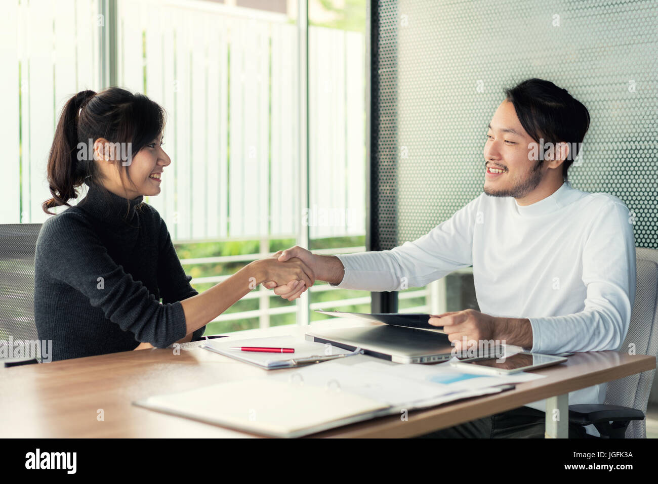 Paio di Asian business persone con abbigliamento casual parlando con felice e agitando la mano in un ufficio moderno o coffee shop. Business il concetto di successo Foto Stock