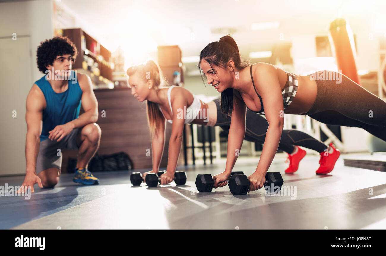 Due ragazze sorridenti esercizi in palestra con personal trainer. Foto Stock