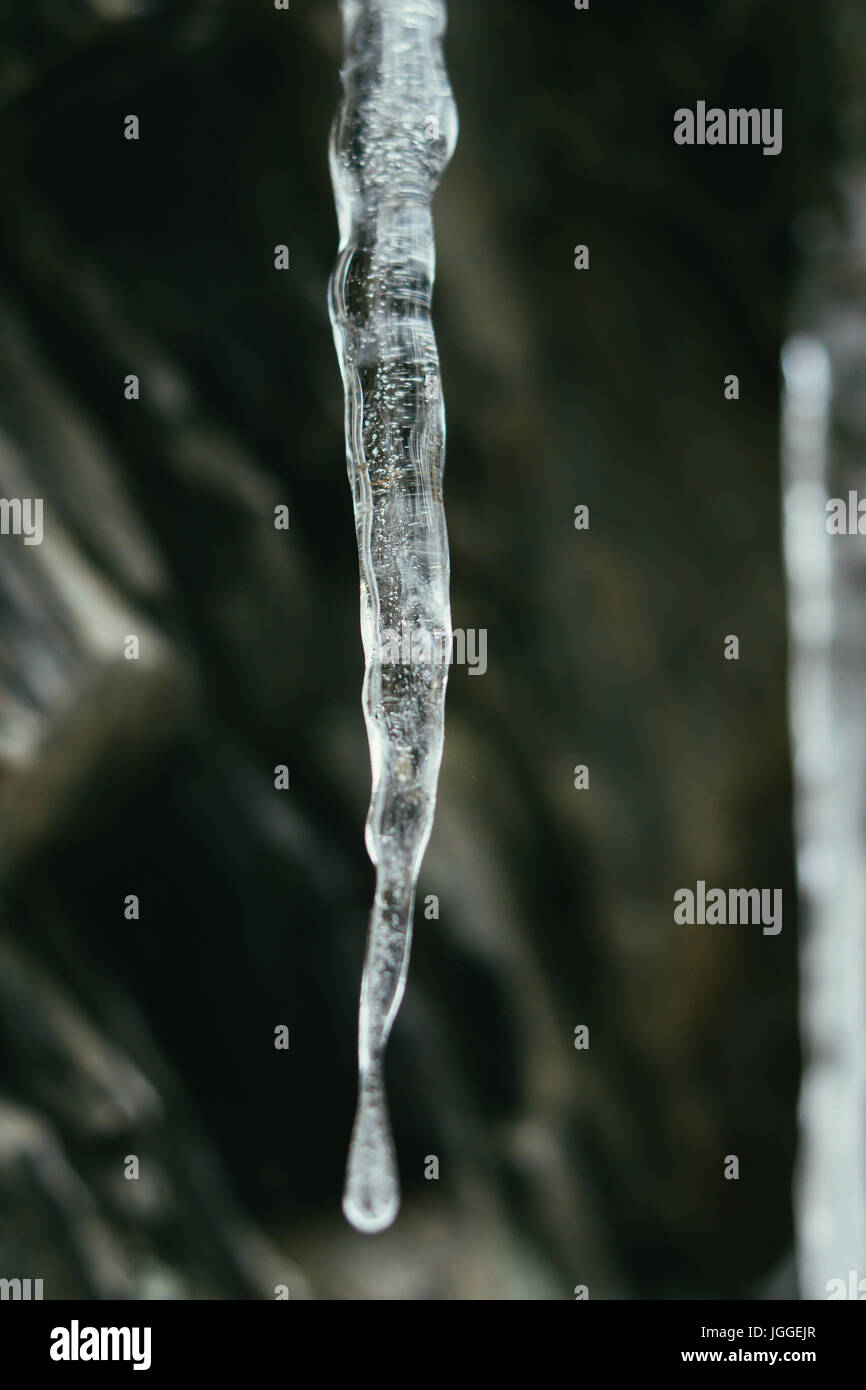 Primo piano di un ghiacciolo trasparente con una goccia di acqua appeso. Foto Stock