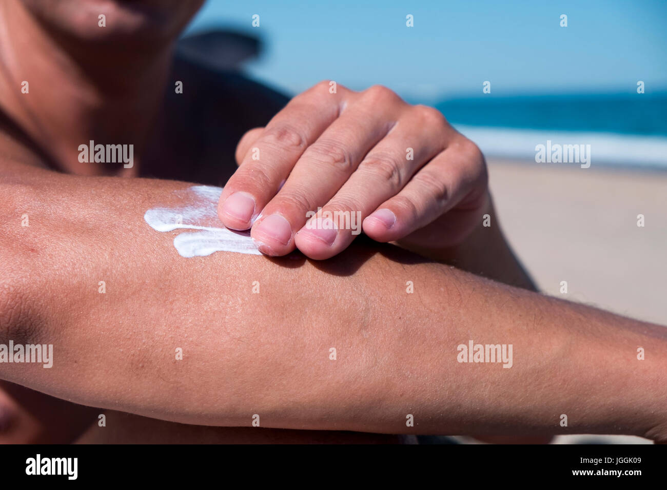 Primo piano di un giovane uomo caucasico sulla spiaggia uomo l'applicazione di crema solare per il suo braccio Foto Stock