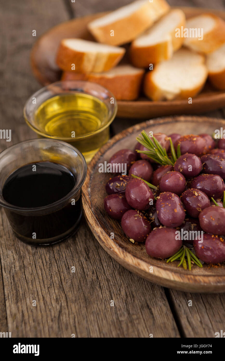 Close up di olive da olio nel contenitore con il pane in background sul tavolo di legno Foto Stock
