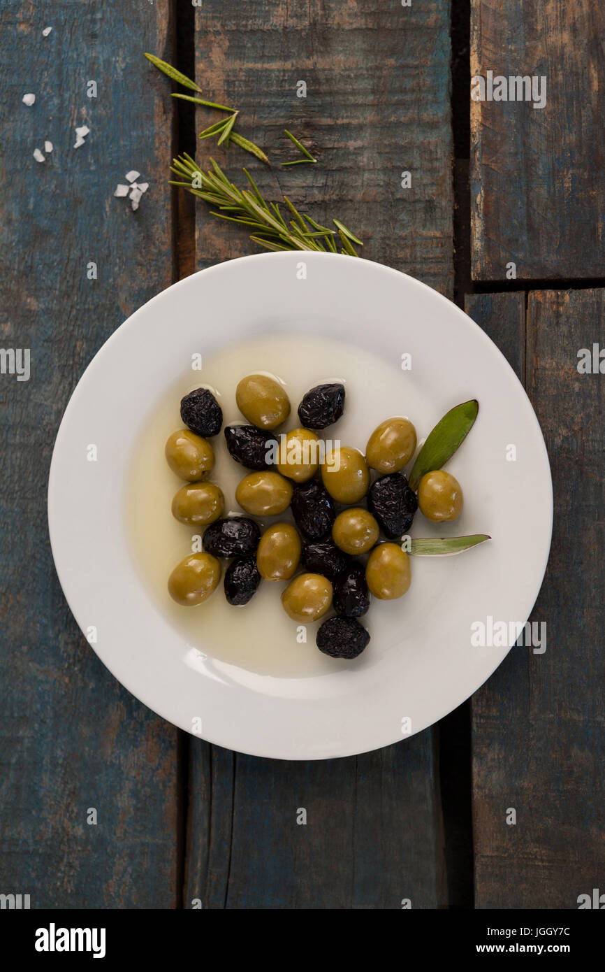 Vista aerea di olive nella piastra con olio su tavola in legno Foto Stock