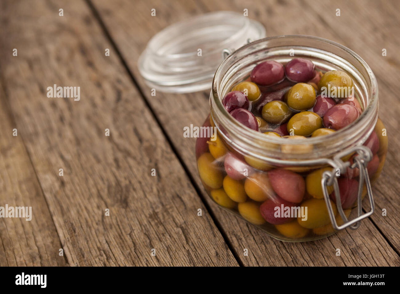 Close up di olive con olio in un barattolo di vetro sul tavolo di legno Foto Stock