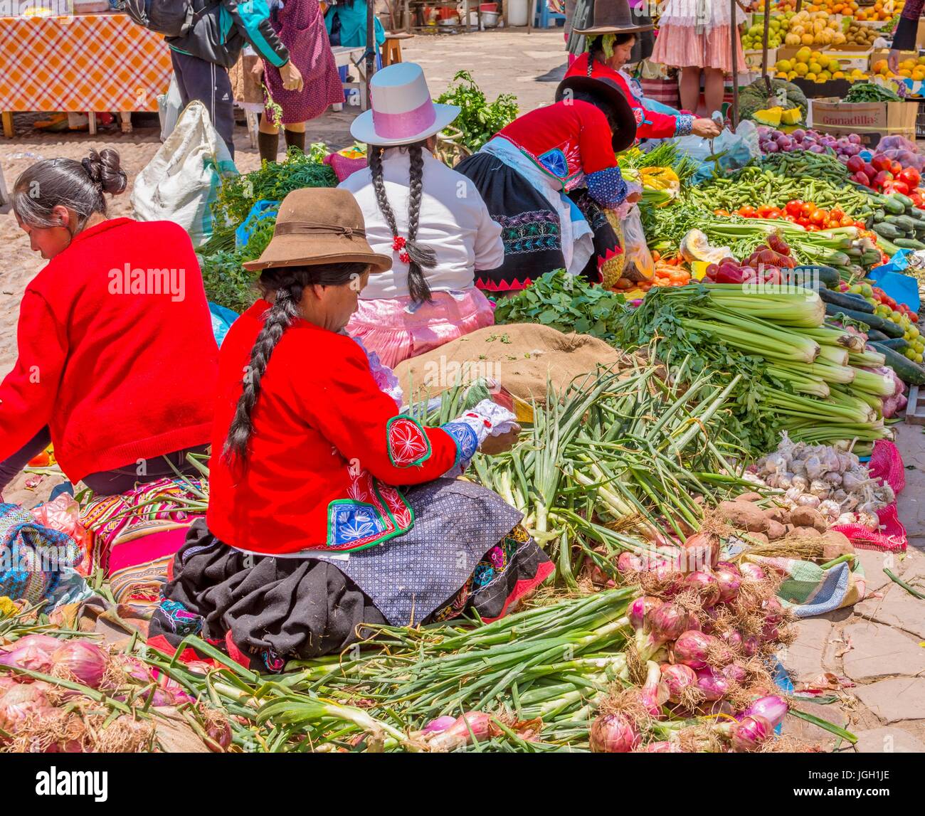 Pisac Perù mercato, locali Peruviani donne con capelli intrecciati, cappelli e indossando abiti tradizionali, vendere la verdura al mercato di Pisac,