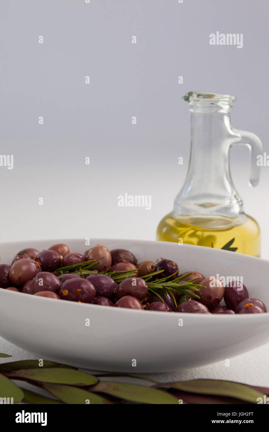 Il rosmarino con le olive in un recipiente da vaso olio su tavola contro la parete Foto Stock