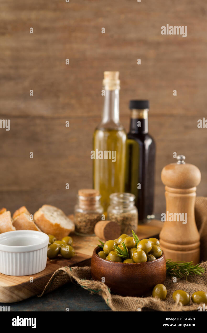 Le olive in un recipiente con bottiglie di olio su tavola contro la parete in background Foto Stock