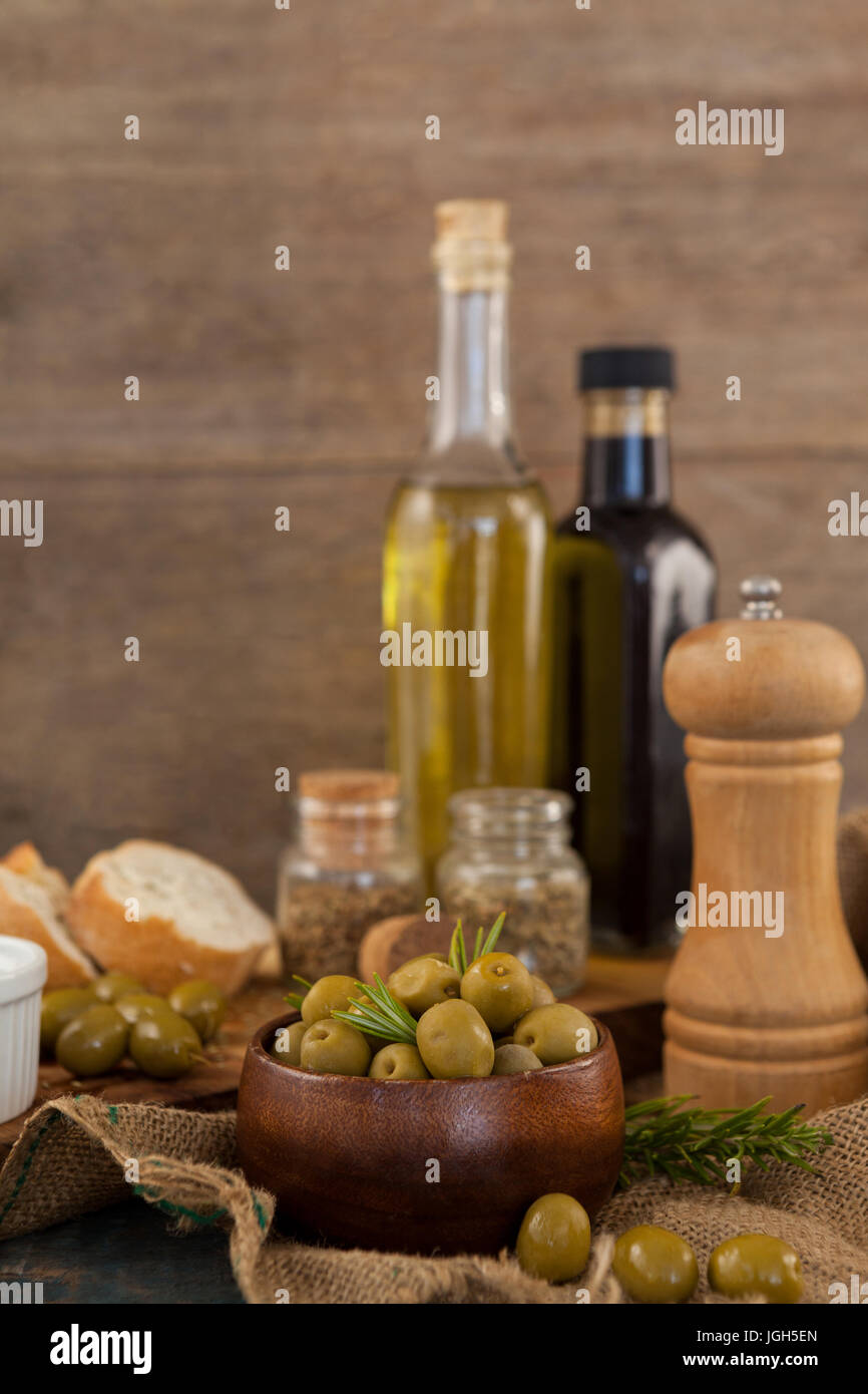 Olive verdi in ciotola con bottiglie di olio su tavola contro la parete in background Foto Stock