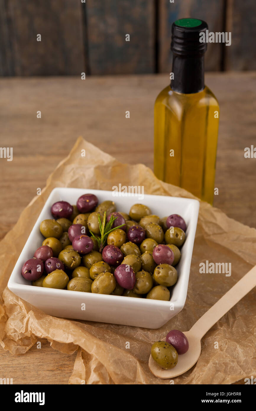 Angolo di alta vista di olive con rosmarino servito in tazza dalla bottiglia di olio su tavola Foto Stock