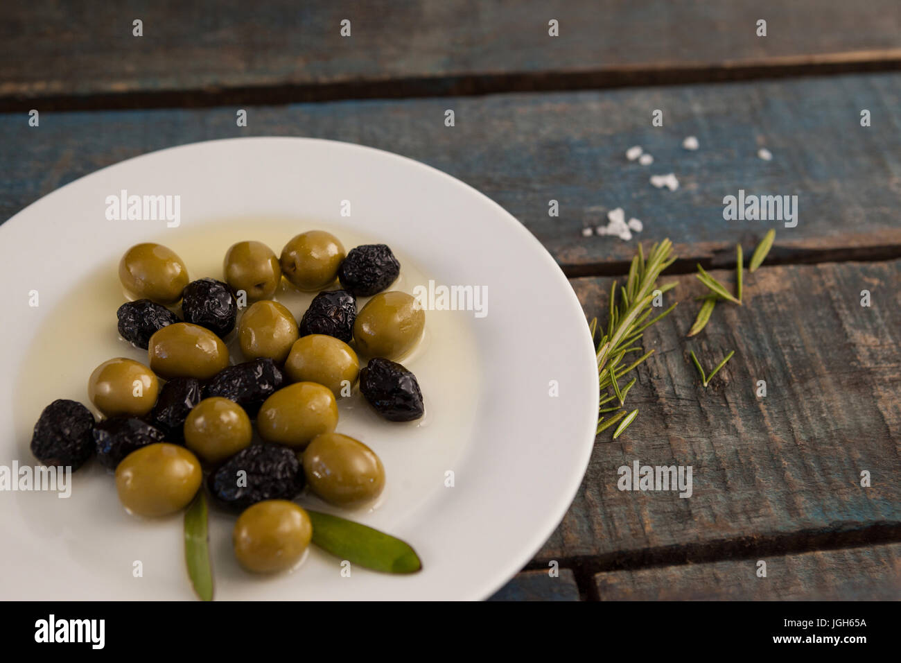 Elevato angolo di vista verde e secca di olive nere con olio nella piastra sulla tavola di legno Foto Stock