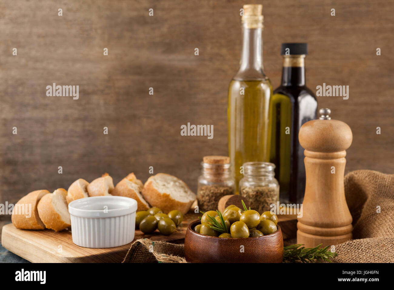 Le olive con pepe shaker e bottiglie di olio mediante il pane sulla tavola contro la parete Foto Stock