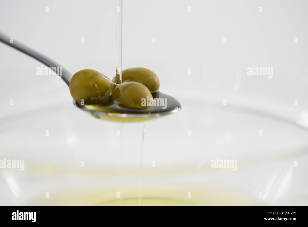 Olio di olive verdi che viene versato in cucchiaio contro uno sfondo bianco Foto Stock