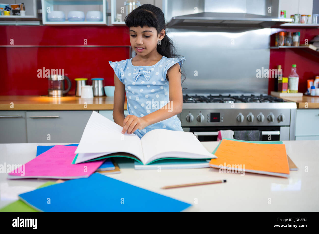 Ragazza flipping pages del libro in cucina a casa Foto Stock