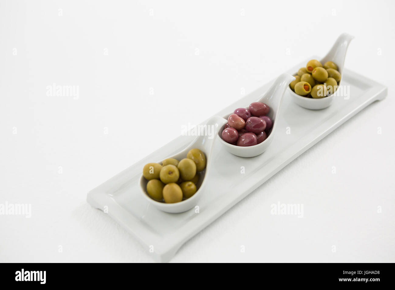 Vari tipi di olive in cucchiaio sul vassoio di portata contro uno sfondo bianco Foto Stock