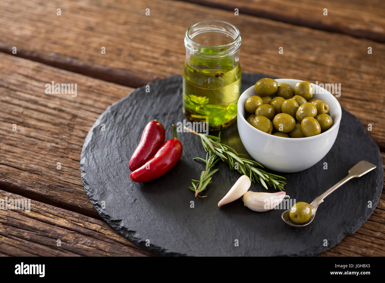 Close-up di olive verdi, erbe aromatiche fresche con olio di oliva e peperoncini rossi su tavola Foto Stock