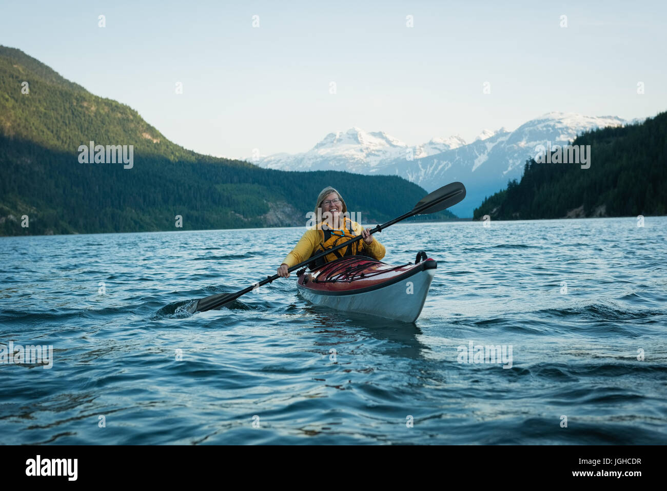 Donna felice oaring mentre kayak nel lago contro sky Foto Stock