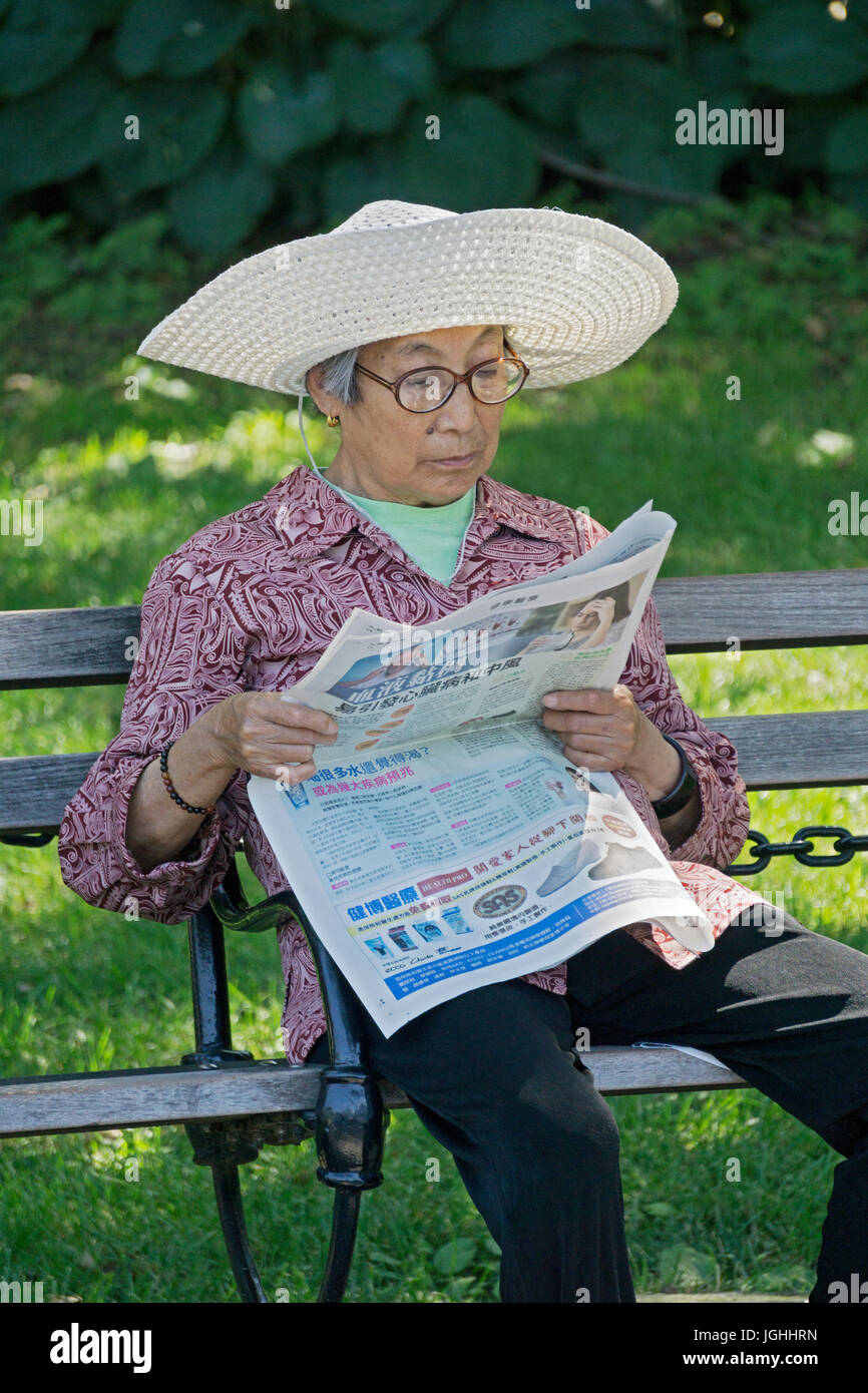 Un americano asiatico donna in un floppy hat leggendo un giornale in Washington Square Park a Manhattan, New York City. Foto Stock