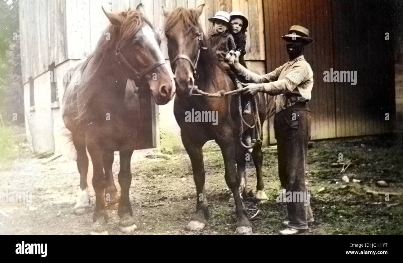 Afro-americano di uomo aiutando due giovani bambini caucasici sul retro di un grande progetto di cavallo, l'uomo sorridente e tenere le redini del cavallo, 1930. Nota: l'immagine è stato colorizzato digitalmente usando un processo moderno. I colori possono non essere periodo-precisa. Foto Stock