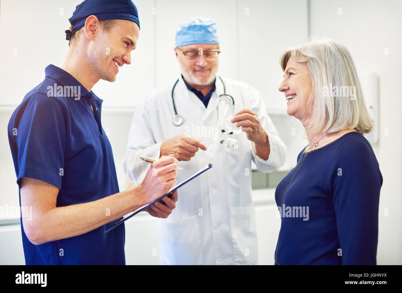 Senior medic consulting femmina adulta del paziente mentre il giovane assistente sorridente permanente e la scrittura nel tablet. Foto Stock