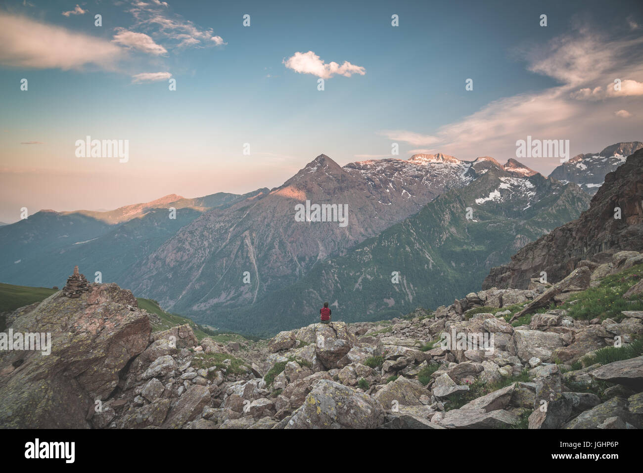 Una persona seduta su terreno roccioso e la visione di un colorato sunrise in alto nelle Alpi. Ampio angolo di visione da sopra con incandescente picchi di montagna nel Foto Stock
