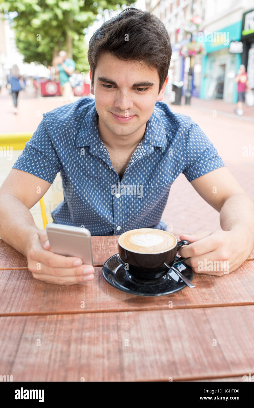 Giovane uomo a Outdoor Cafe scrivere messaggi su telefono cellulare Foto Stock