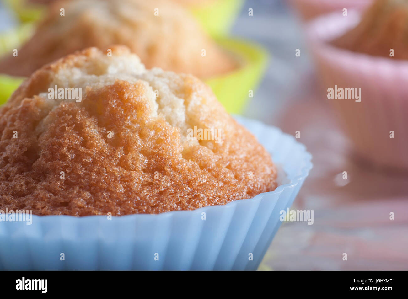 Close up (macro) di plain vanilla tortine in luminosi colori pastello custodie in silicone, pane appena sfornato, non decorato e poggiante su una lamina coperto vassoio da forno. Foto Stock