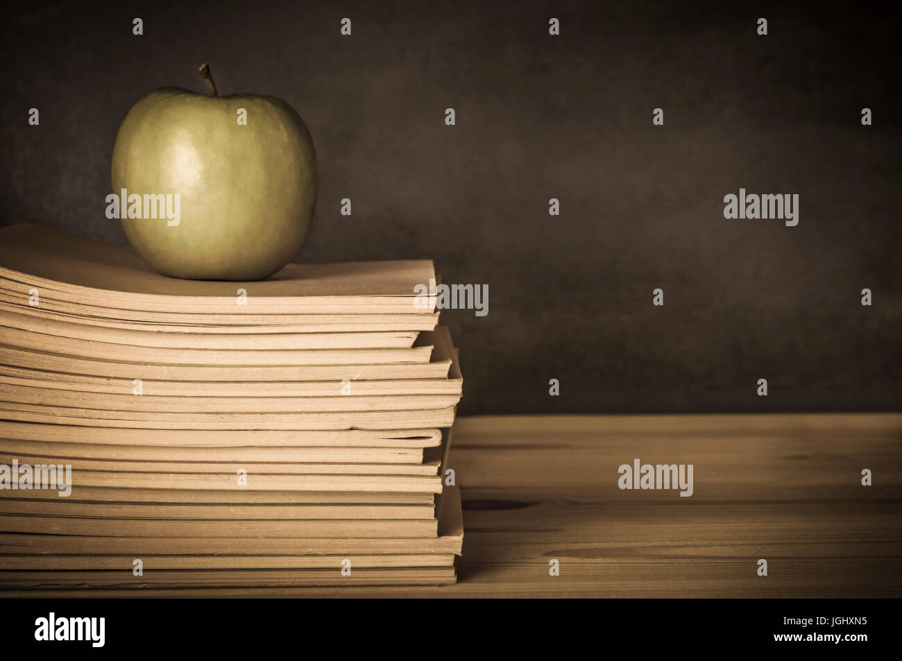 In stile vintage immagine di un insegnante del desk in legno, con un Apple sulla cima di un palo di usato, usurato quaderni. Blackboard nella messa a fuoco morbida dello sfondo. U Foto Stock