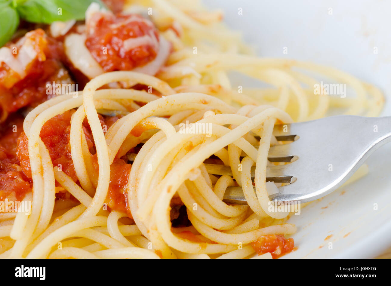 Una ciotola di pasta, la salsa di pomodoro e le foglie di basilico con formaggio. Close-up di avvolgimento a forcella e sollevamento di spaghetti in primo piano. Foto Stock
