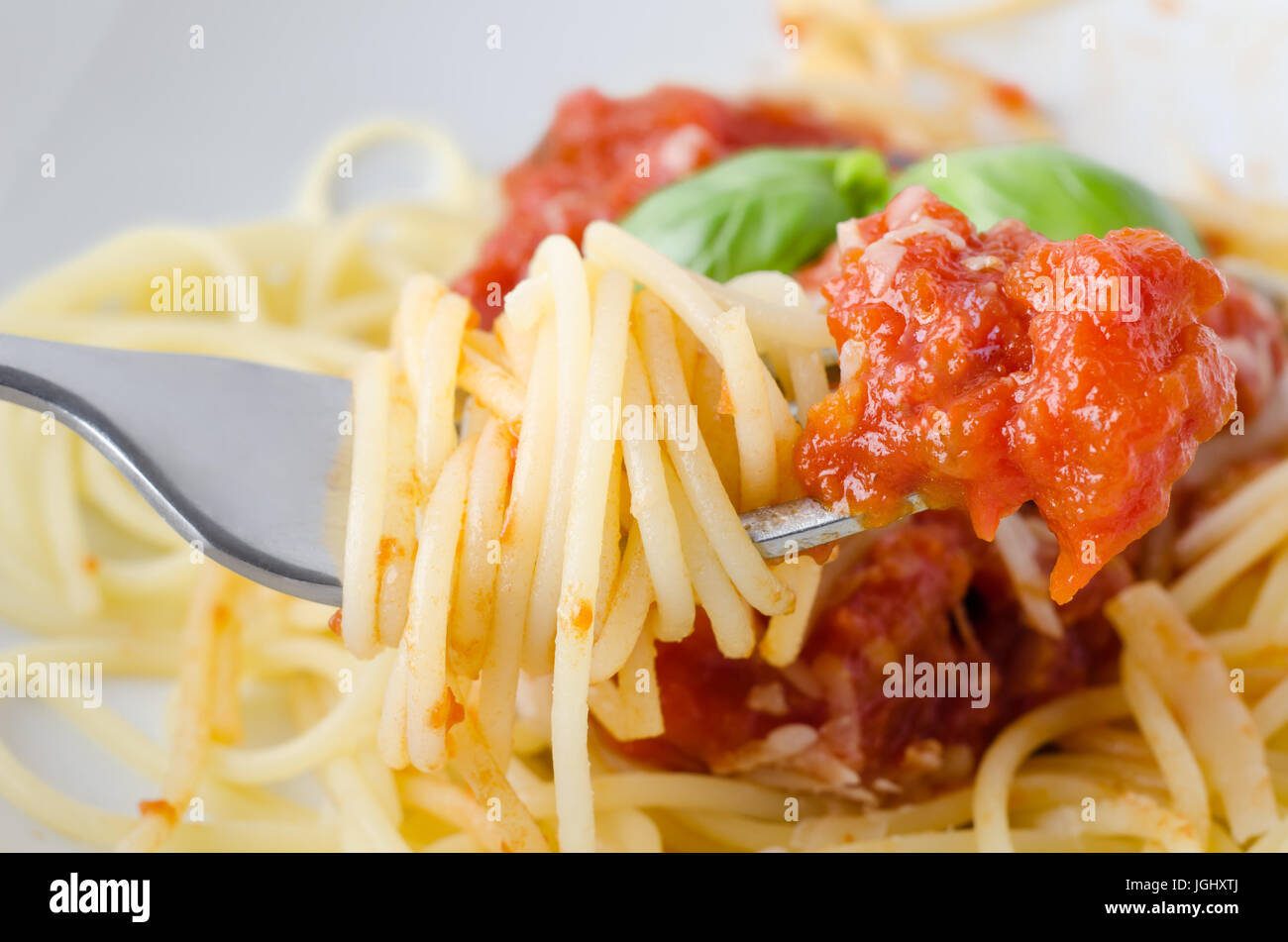 Una ciotola di spaghetti, la salsa di pomodoro e le foglie di basilico con il formaggio, con close-up di forca sollevata in primo piano, avvolto in spaghetti e immerso in s Foto Stock