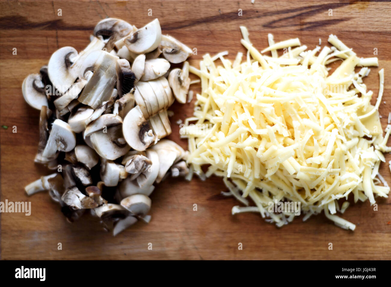 Grattugiato fresco formaggio giallo e un trito di funghi prataioli su un rustico tagliere di legno Foto Stock