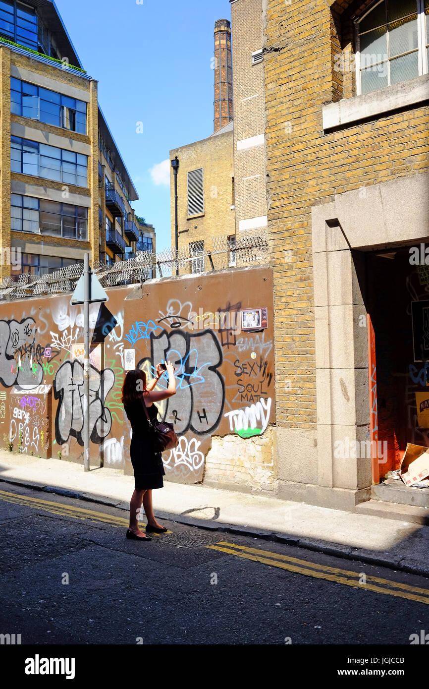 Persona prendendo fotografie dei graffiti in Corbet posto vicino a Brick Lane, Shoreditch, London E1, utilizzando il suo smartphone Foto Stock