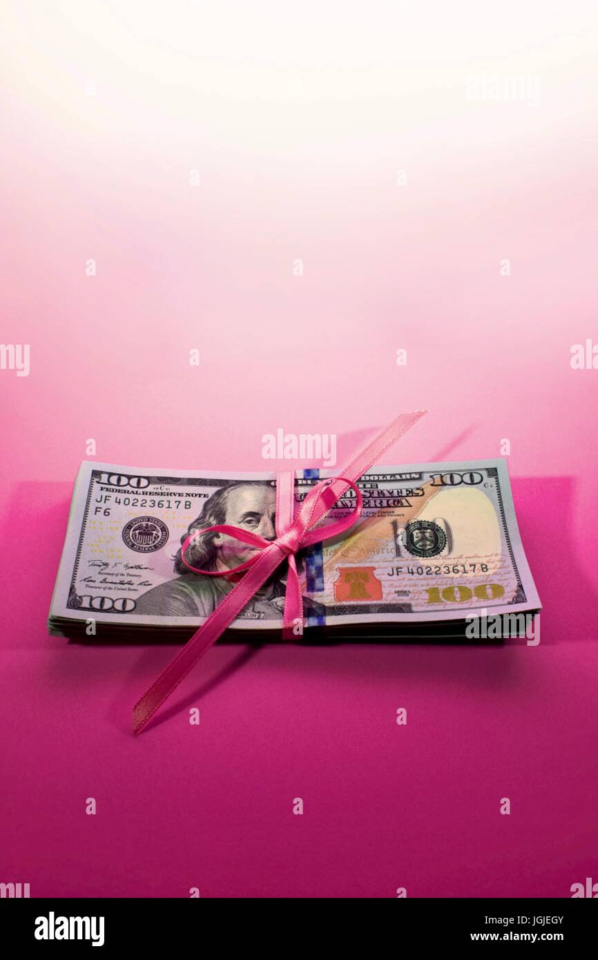 Pila di nuovo Hundred Dollar Bills contanti 100 USD soldi americani su un sfondo rosa tenute insieme con il nastro rosa legato in un arco Foto Stock