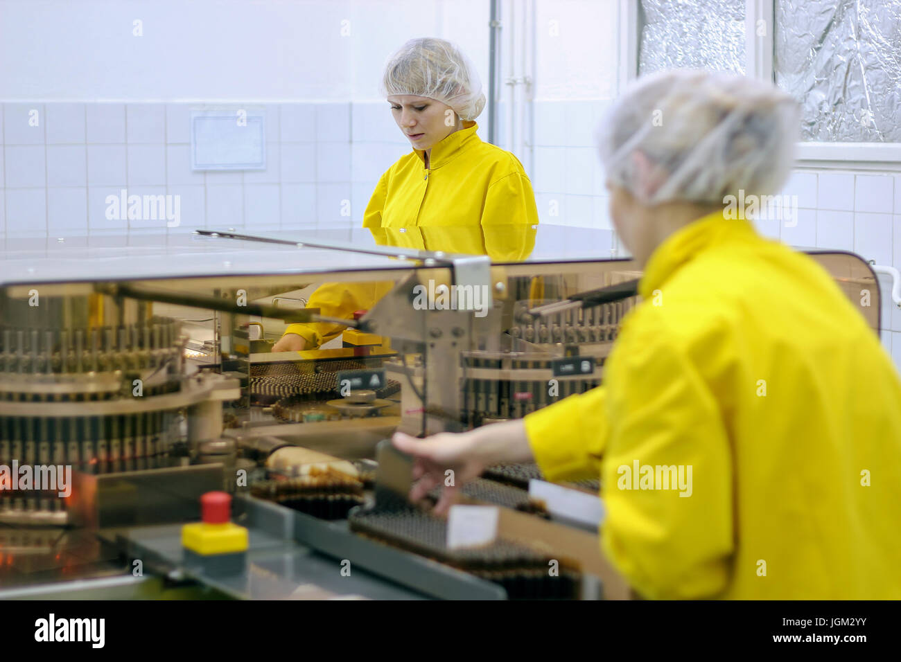 Due fabbrica farmaceutica lavoratori protezione da indossare indumenti da lavoro. I lavoratori di sesso femminile accanto a fiala inspetion ottica macchina alla fabbrica farmaceutica. Foto Stock