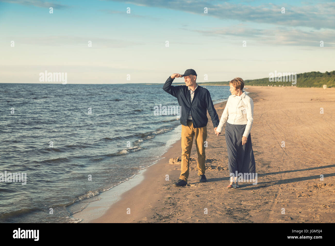 Coppia di anziani avente romantica passeggiata sulla spiaggia al tramonto Foto Stock