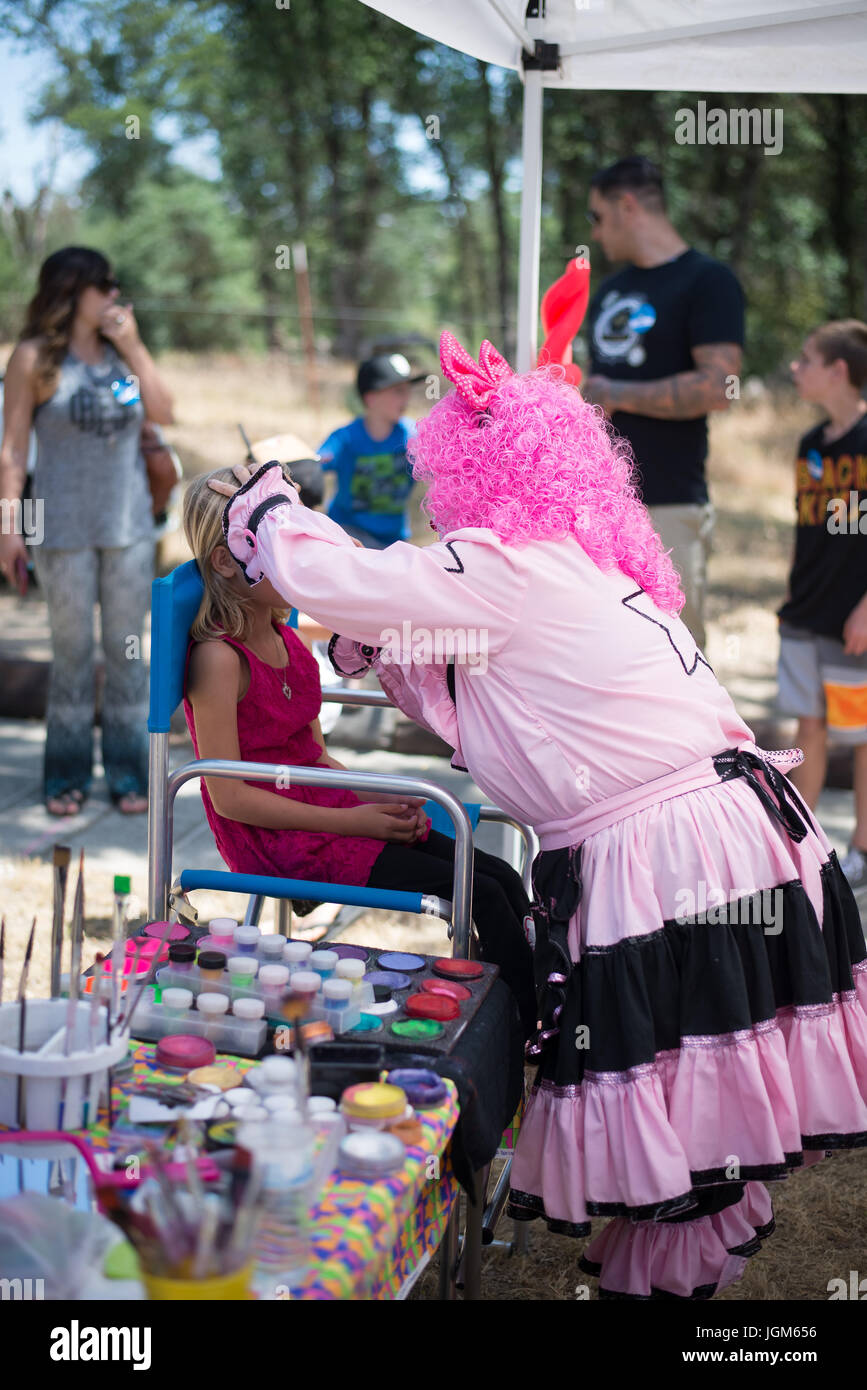 Clown che fornisce facepainting ad un bambino ad un festival Foto Stock