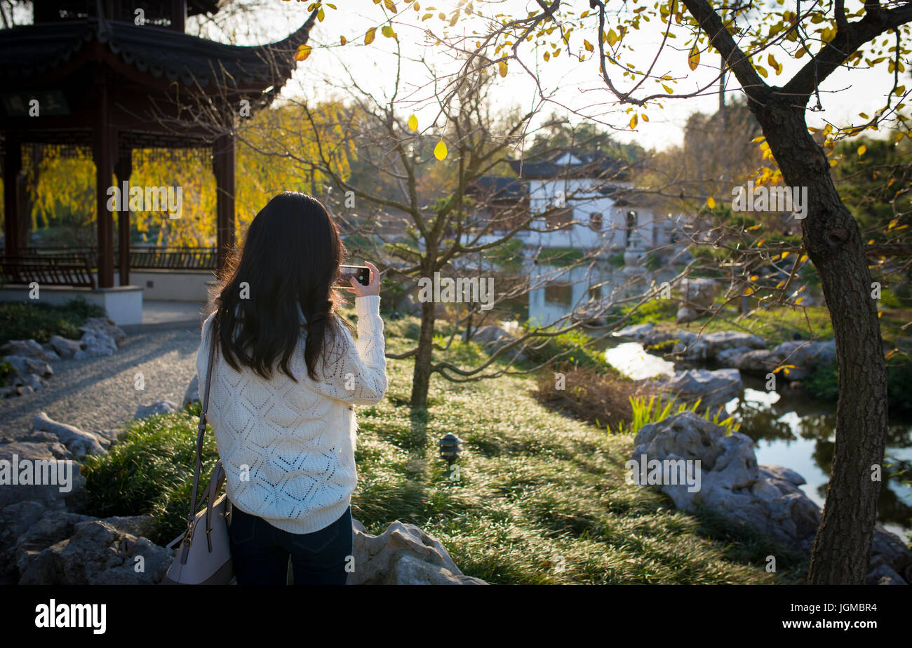 Giovane turista adulta che scatta una foto di un giardino giapponese durante l'ora d'oro Foto Stock