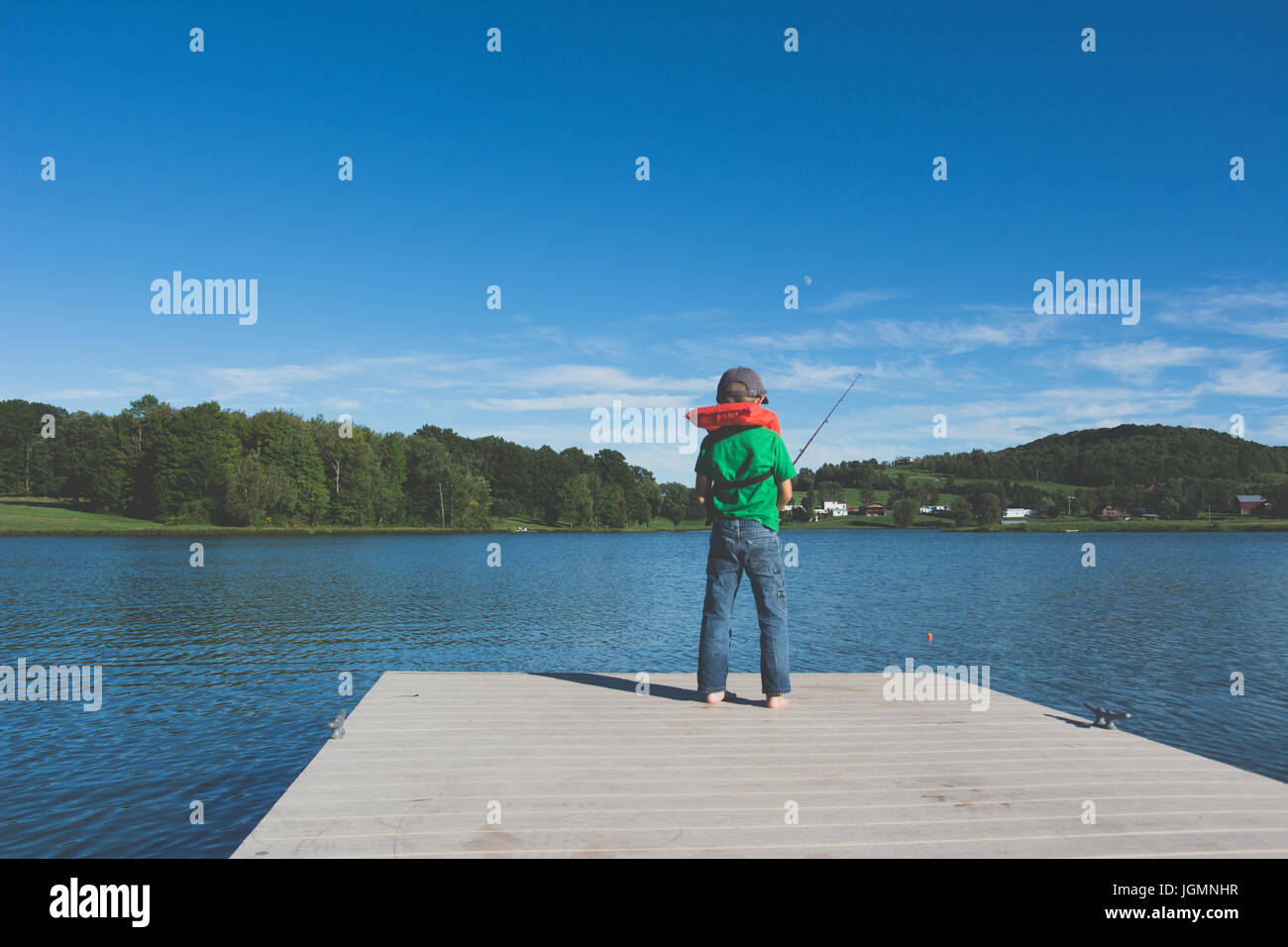 Un bambino la pesca su un dock presso uno stagno in una zona rurale. Foto Stock