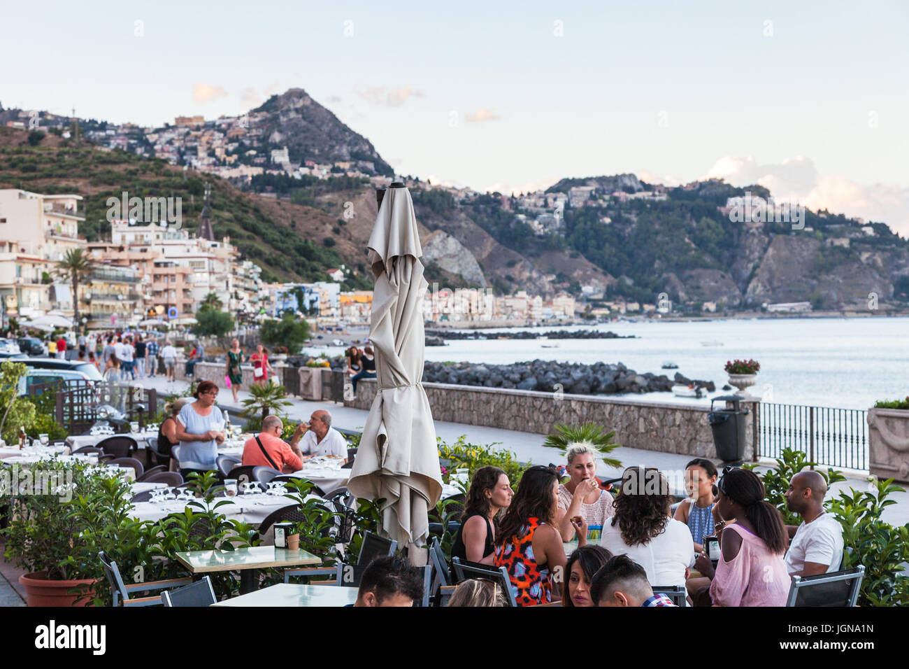 GIARDINI NAXOS, Italia - luglio 2, 2017: persone in marciapiede ristorante sul lungomare di Giardini Naxos town sera d'estate. Giardini Naxos è mare res Foto Stock