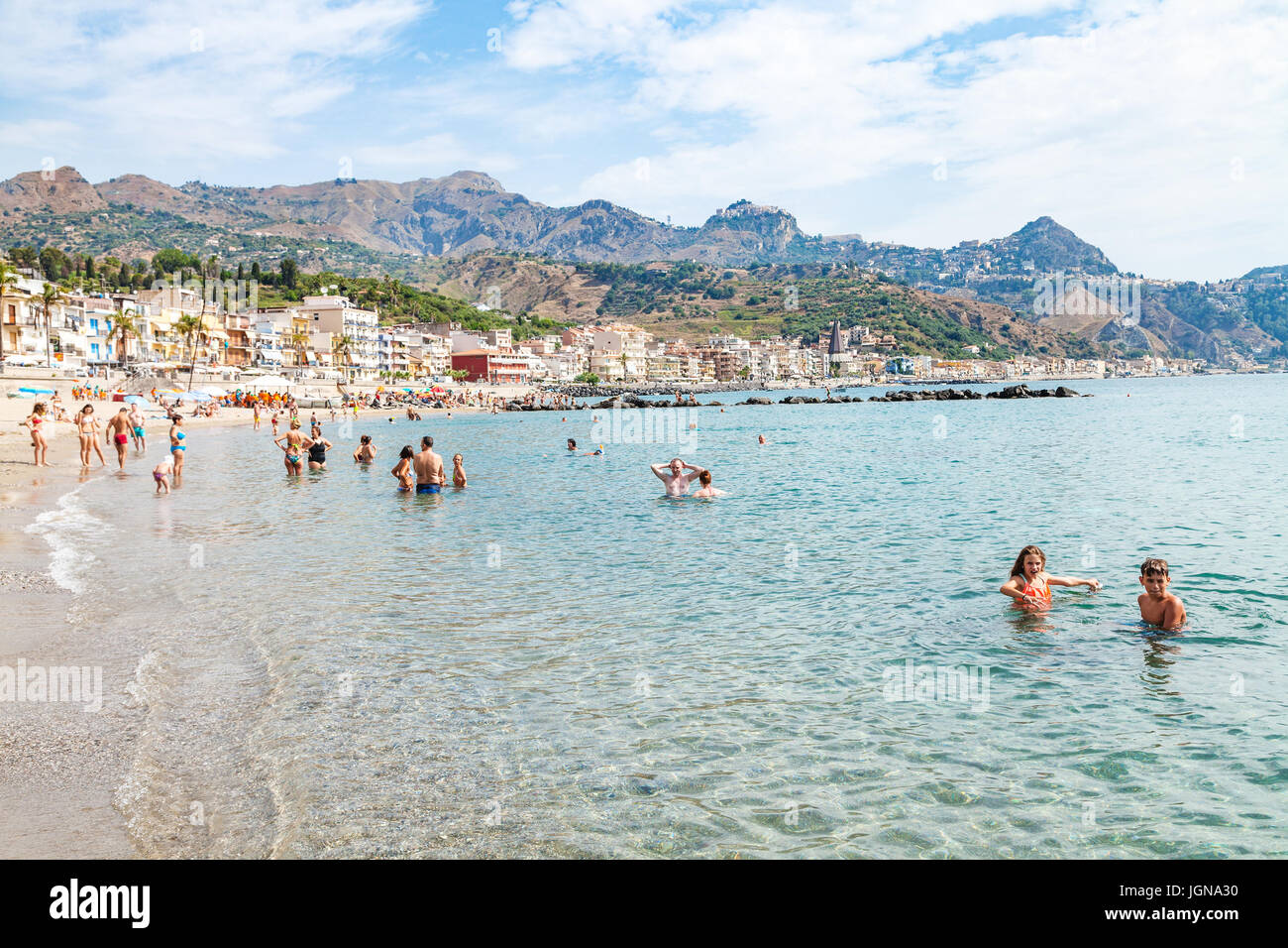 GIARDINI NAXOS, Italia - 28 giugno 2017: persone in mare vicino al lungomare di Giardini Naxos town e vista della città di Taormina sul capo. Giardini Naxos è seasi Foto Stock