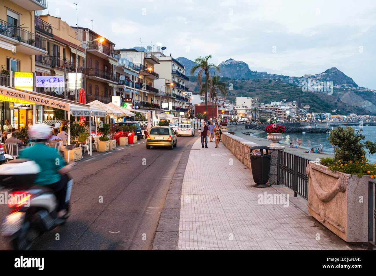 GIARDINI NAXOS, Italia - 28 giugno 2017: persone, negozi e il traffico automobilistico sul lungomare di Giardini Naxos town in serata d'estate. Giardini Naxos è il mare Foto Stock