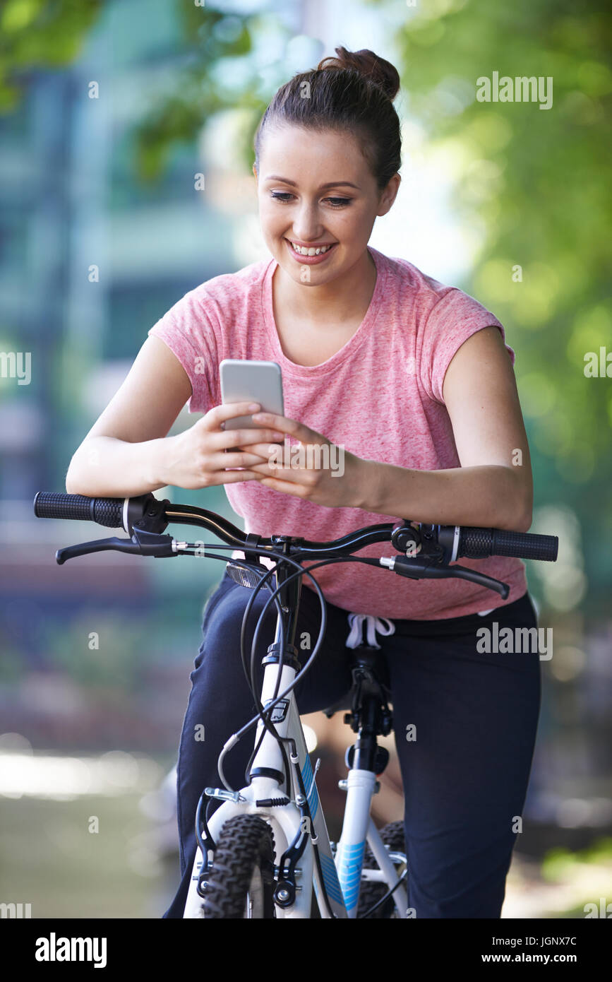 Giovane donna utilizzando il telefono cellulare mentre fuori il giro in bicicletta Foto Stock