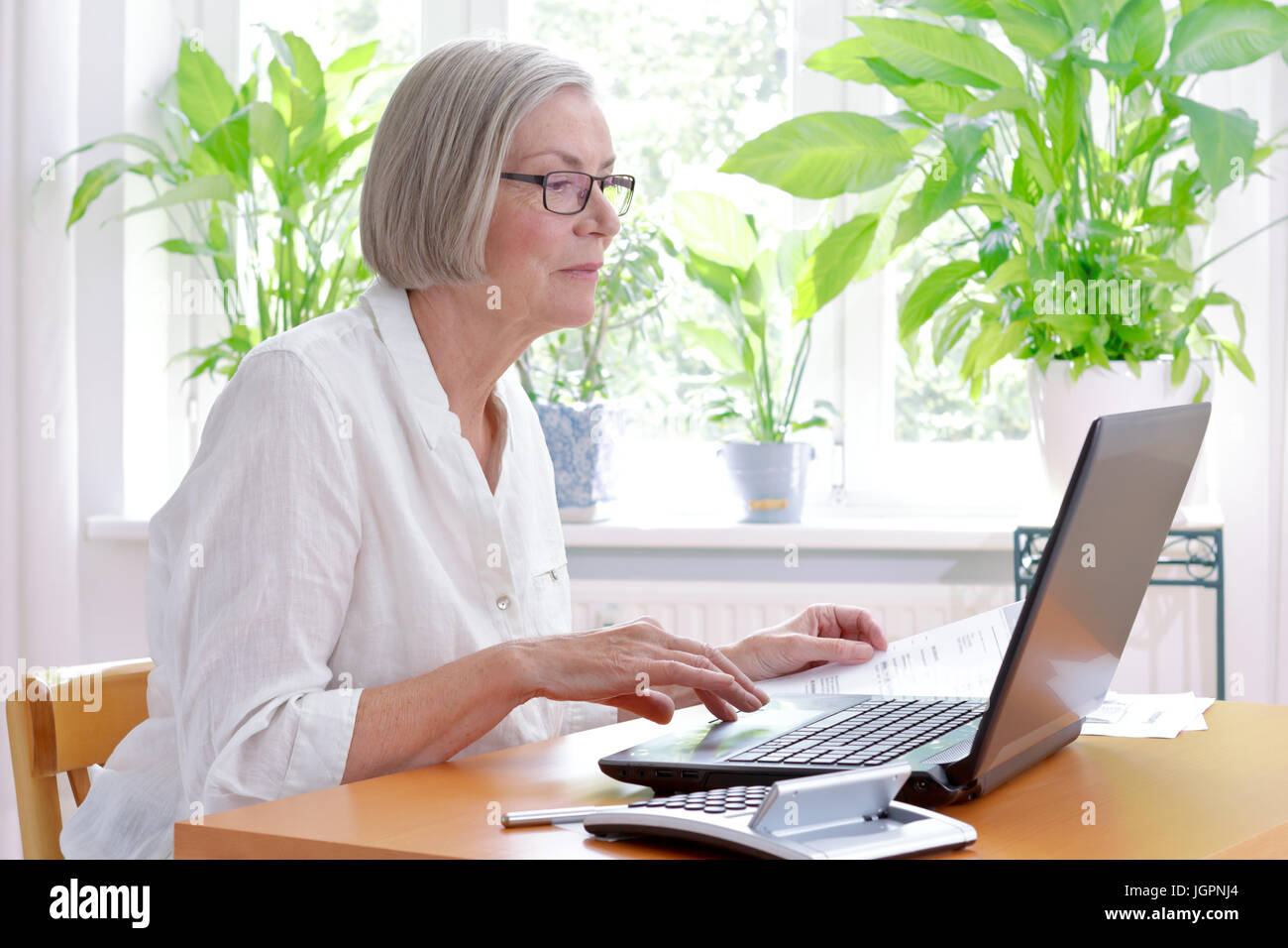 Rilassato donna senior a casa con una calcolatrice e un sacco di ricevute nella parte anteriore del suo computer portatile e rendere la sua annuale dichiarazione fiscale Foto Stock