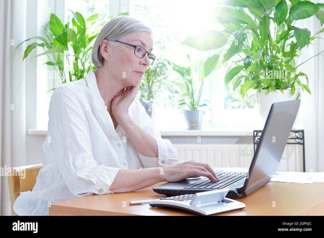 Senior donna nel suo soggiorno Staring irritati con lo schermo del suo computer portatile,computer o problemi finanziari Foto Stock