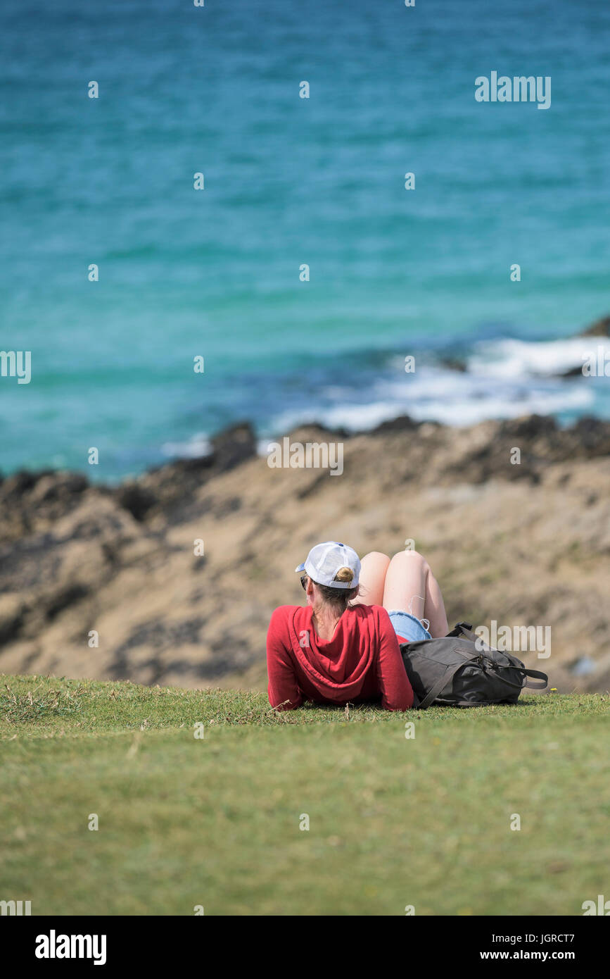 Una giovane donna di rilassarsi al sole sul promontorio in Newquay, Cornwall. Foto Stock
