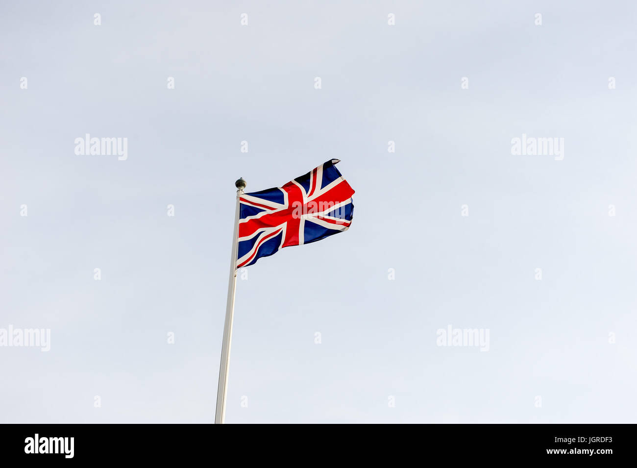 Union Jack flag contro sky svolazzanti su una bandiera bianca pole Foto Stock