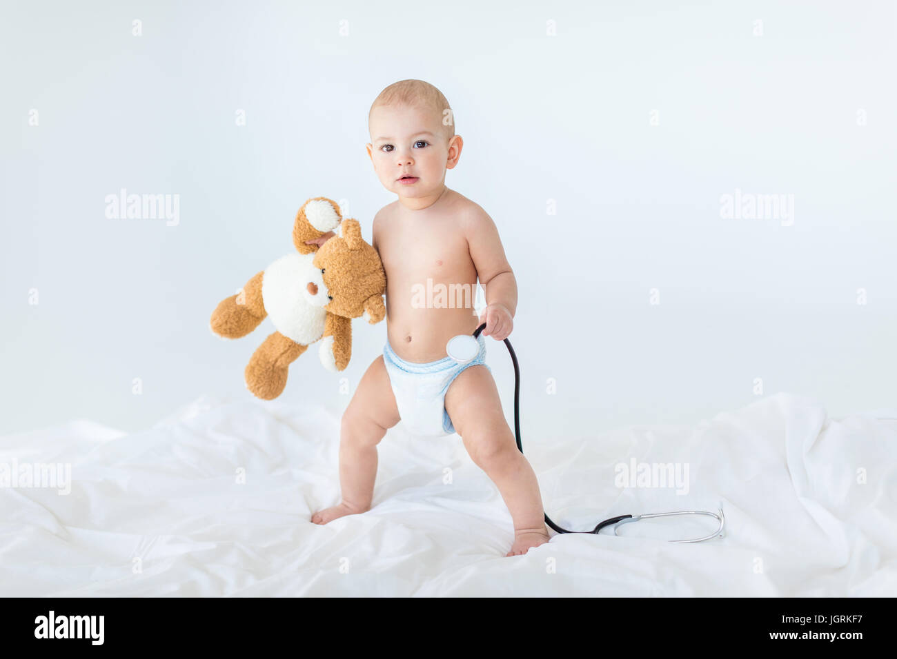 Adorabile piccola baby boy in piedi sul letto e tenendo uno stetoscopio con Teddy bear, 1 anno vecchio concetto di bambino Foto Stock