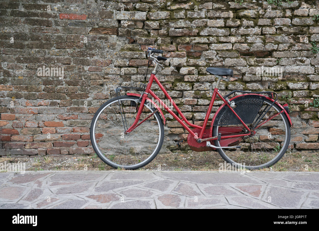 Rosso in bicicletta lungo una parete di mattoni Foto Stock