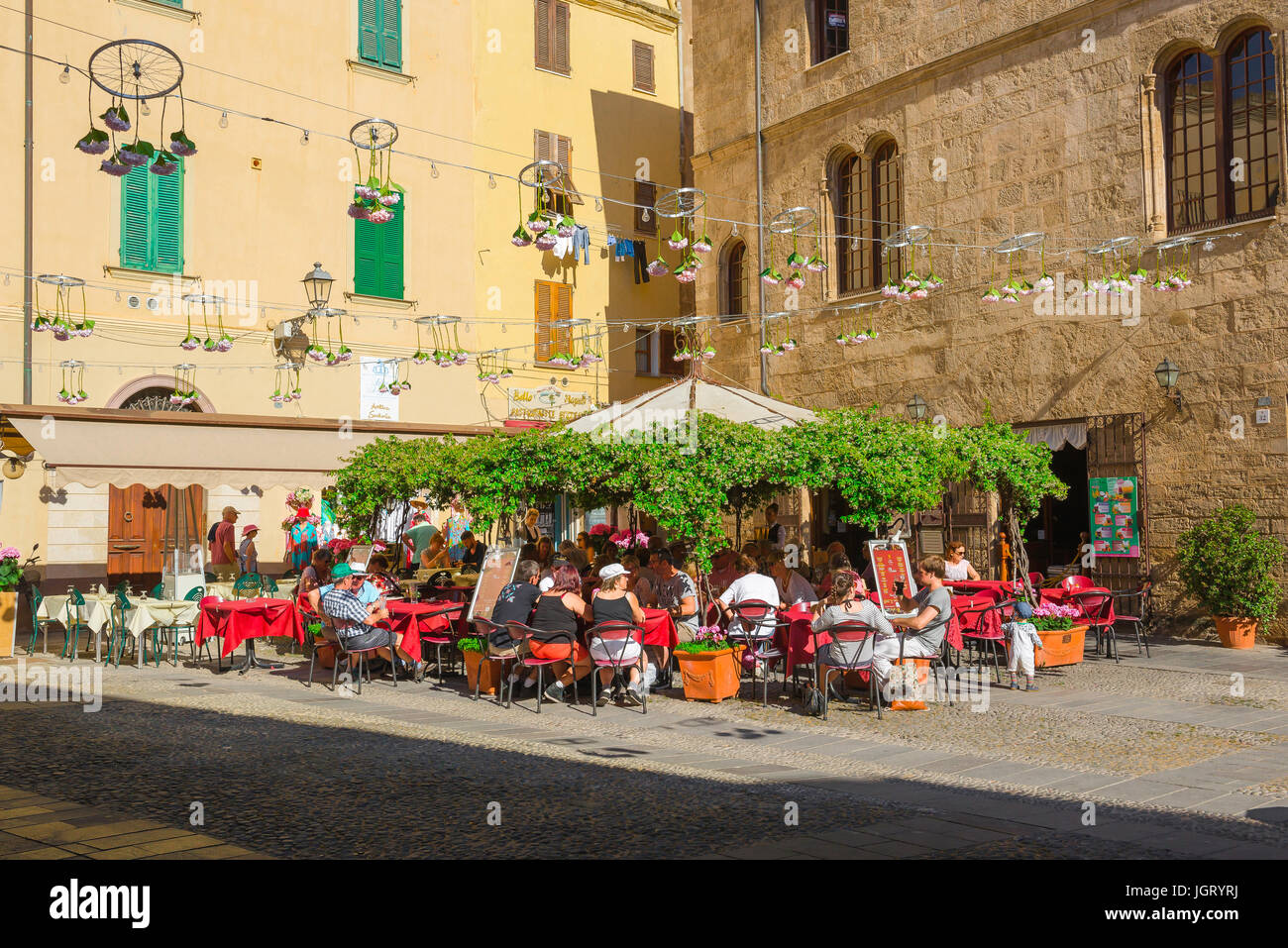 Alghero Sardegna, le persone a rilassarsi presso i tavoli fuori un cafe bar situato in un angolo soleggiato della Piazza Civica di Alghero, Sardegna, Italia. Foto Stock