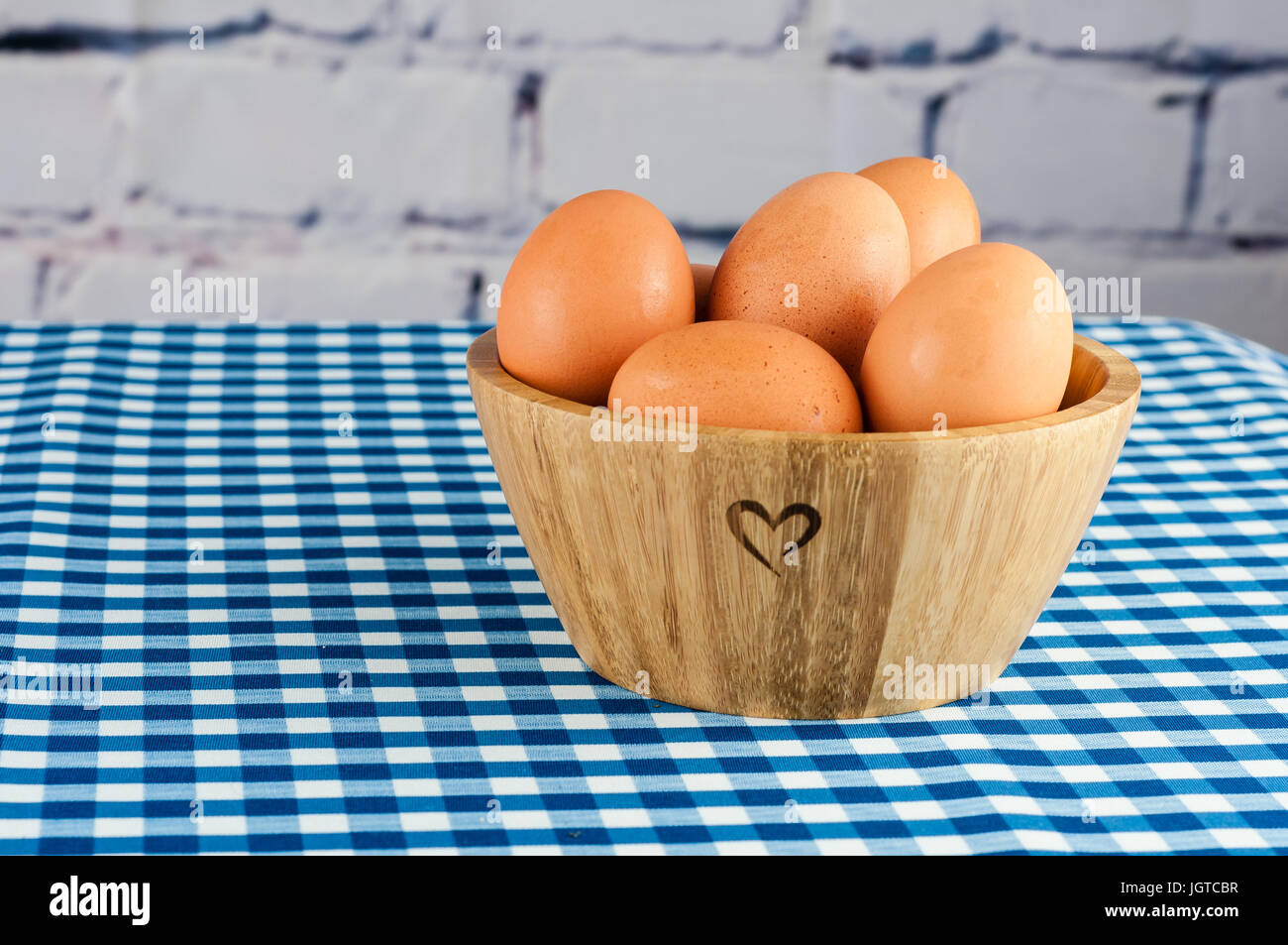 Di uova fresche in una ciotola di legno con a forma di cuore ad incisione su un blu tovaglia gingham Foto Stock