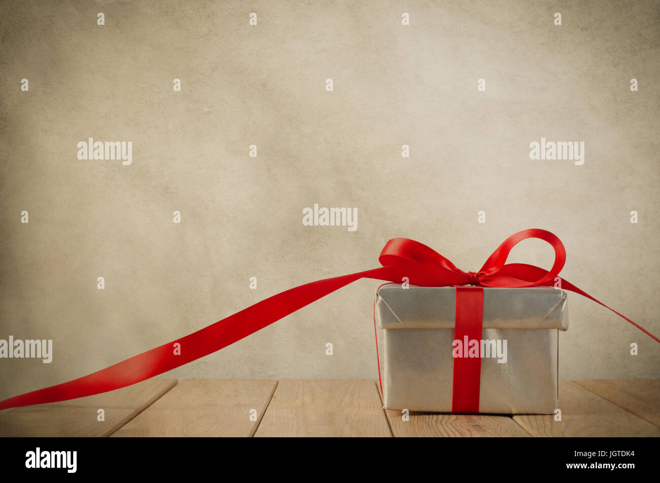 Un argento Confezione regalo con nastro rosso su asse di legno tabella. Percorsi di nastro a lato e le facce anteriore. Vecchia pergamena grungy effetto fornisce un vintage fe Foto Stock