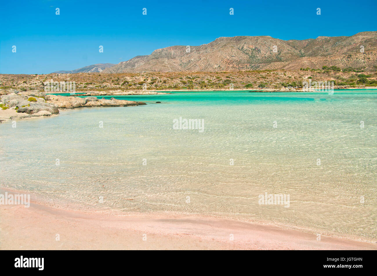 Cancellare le acque poco profonde del mare Mediterraneo nel famoso Elafonisi spiaggia con sabbia rosa e le montagne a sfondo sull isola di Creta sulla soleggiata giornata estiva, Foto Stock